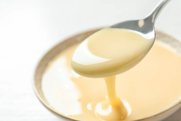 Spoon of pouring condensed milk over bowl on table, closeup with space for text. Dairy products - Valokuva, kuva
