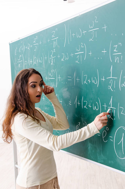 Νεαρή καθηγήτρια μαθηματικών μπροστά στον πίνακα.   - Φωτογραφία, εικόνα