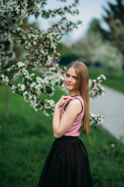 Beautiful blond hair girl standing in front of the blooming tree. Charming lady in dress - Foto, Imagem