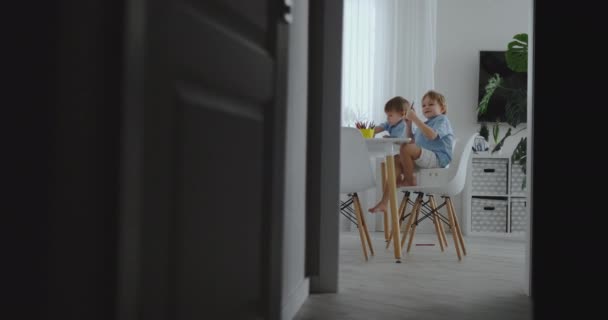 Onnellinen perhe nuori kaunis äiti ja kaksi poikaa piirtää värillisiä kyniä istuu pöydässä keittiössä. Kamera liikkuu hidastettuna.
 - Materiaali, video