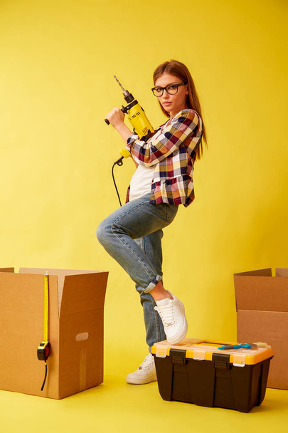 Young woman holding a drill, standing between the boxes for moving. Studio - Foto, immagini
