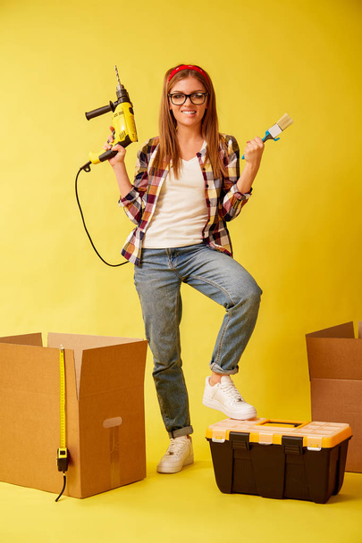 Woman skillfully holds a drill and a paint brush, standing between the boxes. Studio - Valokuva, kuva