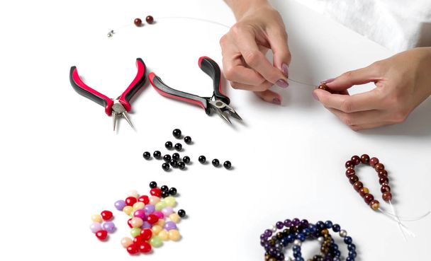 Kleurrijke kralen armband te maken. Vrouwelijke handen met een gereedschap op een witte achtergrond. Selectieve aandacht - Foto, afbeelding