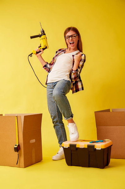 Young woman holding a drill, standing between the boxes for moving. Studio - Fotoğraf, Görsel