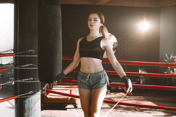 Young athletic woman exercising using skipping rope on boxing ring gym background. Fitness concept. Healthy lifestyle. Young slim woman jumping with skipping rope in gym. - Photo, Image