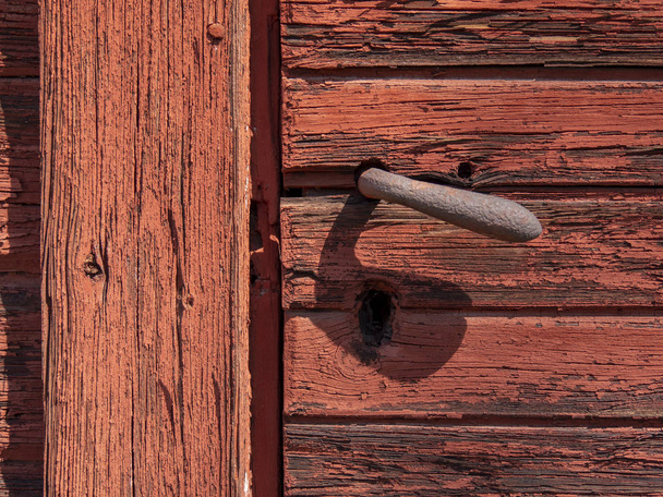Close-up van een houten deur gelakt rood met een metalen handvat - Foto, afbeelding