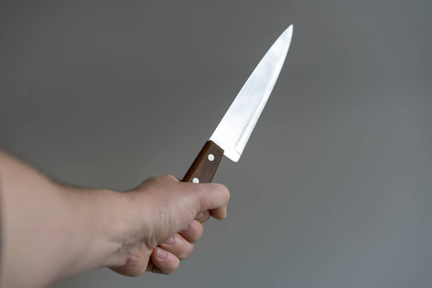 Mano de hombre con un cuchillo sobre fondo gris. Concepto de violencia
 - Foto, Imagen