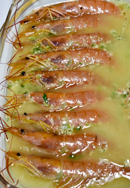 a tray of glass full of shrimps cooked with a tasty sauce of garlic, oil and parsley ready to be eaten on a table. Vertical photo. - Photo, Image