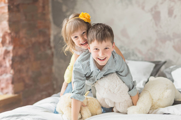 Brother and sister playing with teddy bear in bed - Фото, изображение