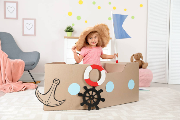 Cute little girl playing with cardboard ship at home - Фото, зображення