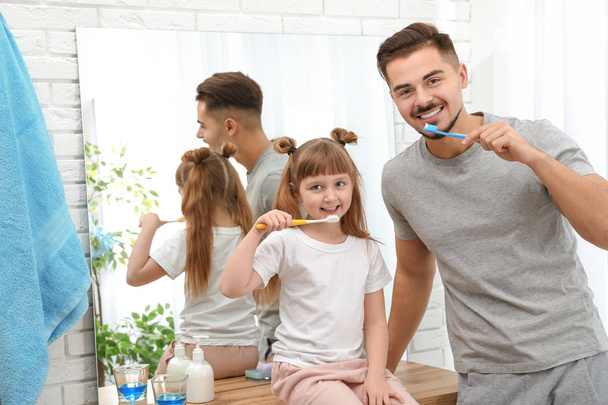 Little girl and her father brushing teeth together in bathroom at home - Foto, imagen