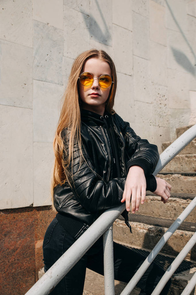 Fashion portrait pretty teenager girl in sunglasses and black rock style over city background - 写真・画像