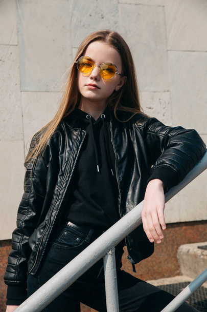 Fashion portrait pretty teenager girl in sunglasses and black rock style over city background - Фото, изображение
