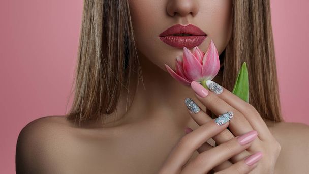 Piękno portret młodej kobiety z kwiatem. Model Dziewczyna z profesjonalny makijaż i manicure paznokci sztuki na różowym tle. - Zdjęcie, obraz