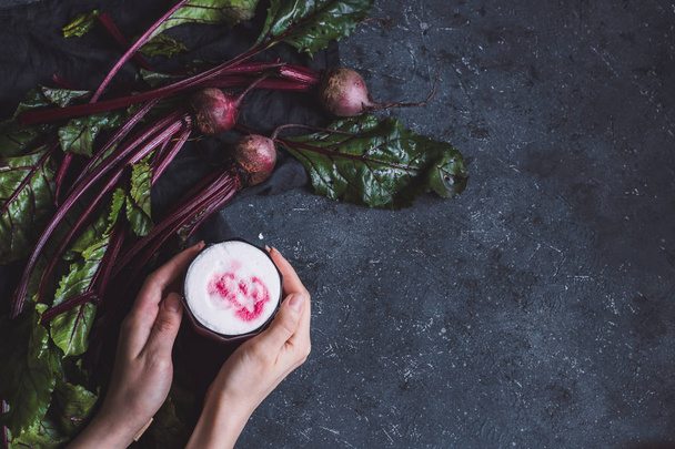 Beetroot drink. Hands holding healthy beetroot latte with whole beetroots on dark background with copy space.  - Foto, Bild