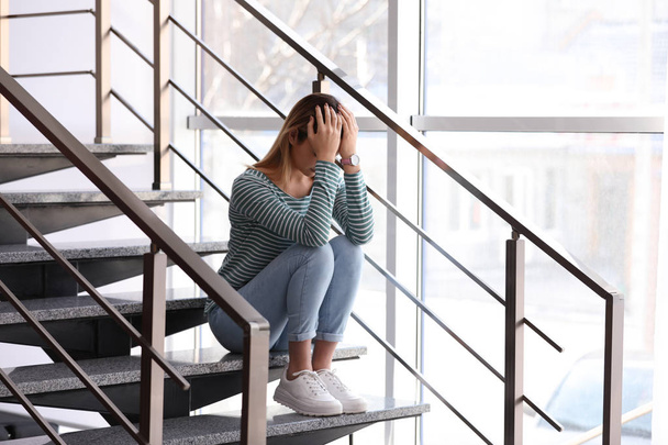Emotional teenage girl sitting on stairs indoors - Photo, image