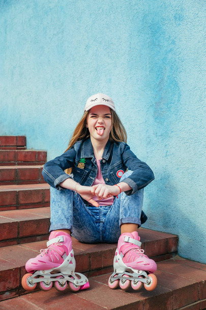 Teenager girl on roller skates sitting on step in city - 写真・画像
