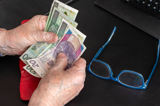 Hands of an elderly pensioner holding leather wallet with polish currency money. Concept of financial security in old age. - Foto, imagen