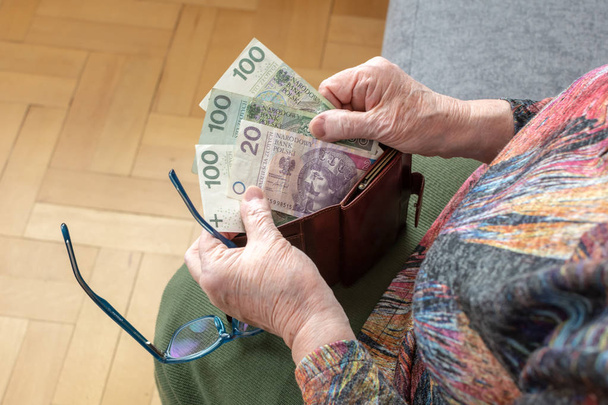 Hands of an elderly pensioner holding leather wallet with polish currency money. Concept of financial security in old age. - Фото, изображение