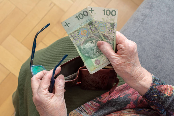 Hands of an elderly pensioner holding leather wallet with polish currency money. Concept of financial security in old age. - Foto, imagen