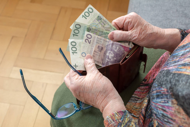 Ręce z podeszłym wieku emeryta, trzymając skórzany portfel z polskiej waluty pieniędzy. Koncepcja bezpieczeństwa finansowego w starszym wieku. - Zdjęcie, obraz