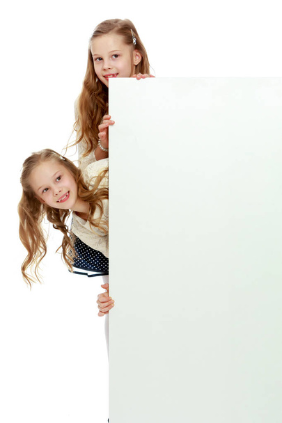 Two little girls peeking out from behind a white advertising ban - Фото, изображение