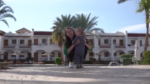 das Baby rennt in Zeitlupe fröhlich zu Mama auf dem Hintergrund des Pools - Filmmaterial, Video