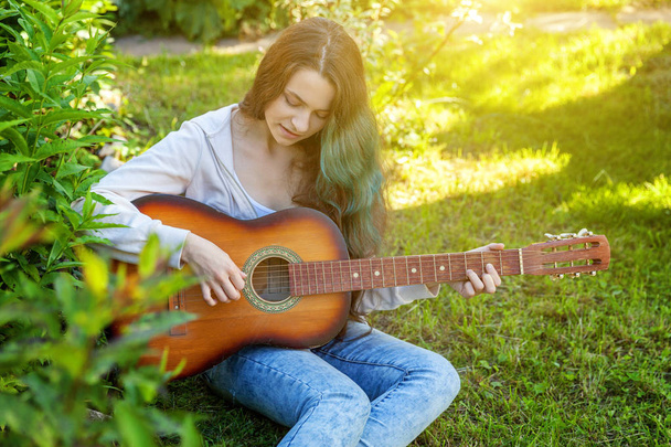 Młoda kobieta siedzi w trawie i gra na gitarze - Zdjęcie, obraz