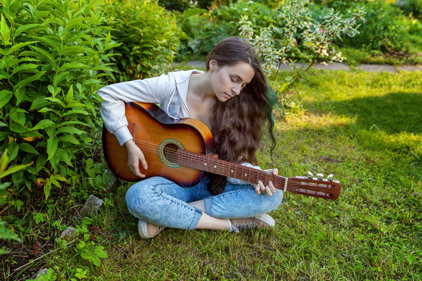Jonge vrouw zitten in het gras en het spelen van gitaar - Foto, afbeelding
