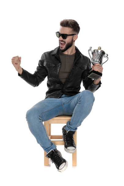 чоловік сидить на стільці кричить з чашкою трофею в руці
 - Фото, зображення