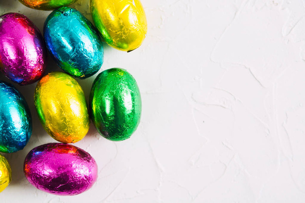 Easter background with colorful chocolate sweet eggs on white textured background - Foto, Bild