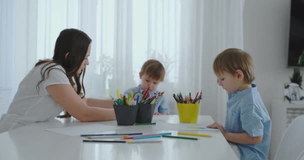 Moeder helpt twee zonen uit te voeren preschool huiswerk om te tekenen van een potlood-tekening aan de tafel in het huis - Video