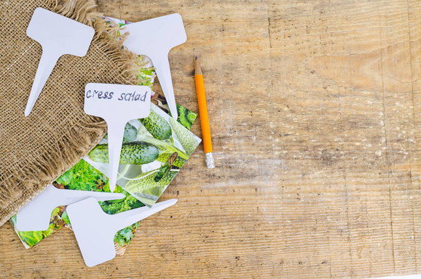 White labels-markers for plants lie on burlap, on wooden  background.  - Photo, Image