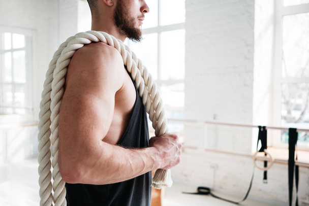 Close up portrait strong fit man with crossfit ropes in cross gym. Muscular athlete holding battle ropes on shoulders in cross hall - Фото, изображение