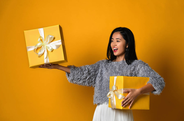 Portrait of a smiling pretty girl holding two gift boxes isolated over yellow background - Foto, imagen