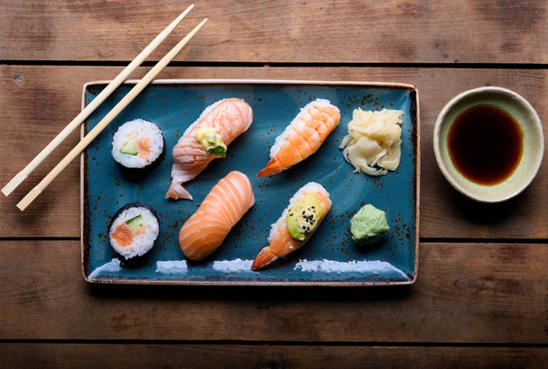 Placa azul com seleção de sushi, pauzinhos e molho de soja em um baú de madeira vintage
 - Foto, Imagem