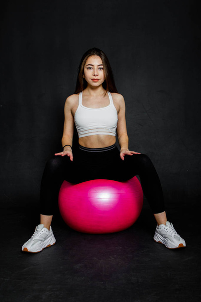 Athletic and strong young woman doing some exercise on the fitness ball on a black background - Valokuva, kuva