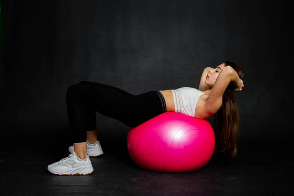 Спортивная и сильная молодая женщина делает некоторые упражнения на фитнес-мяч на черном фоне
 - Фото, изображение