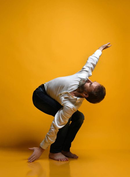 Old man practicing yoga doing stretching exercises against yellow background - 写真・画像