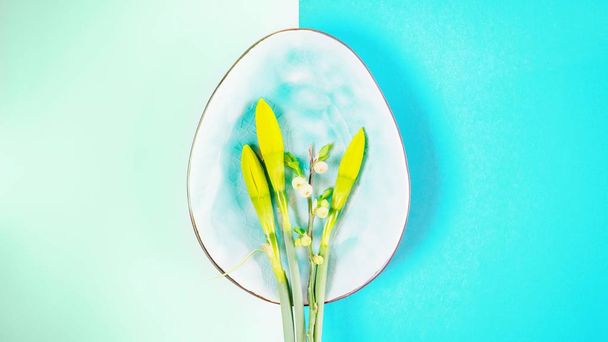 Placa en forma de huevo con brotes narcisos y rama de primavera sobre un color verde mágico y fondo turquesa. 16: 9. Copiar espacio
 - Foto, Imagen