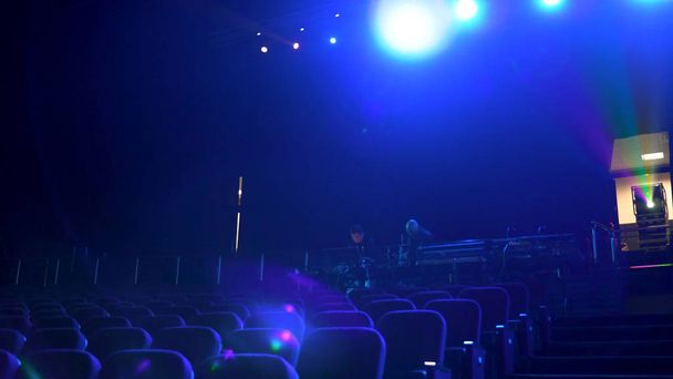 Dark, empty cinema hall with comfortable seats in blue light, projector, and bright spotlights. Close up for seat rows in movie theatre. - Photo, Image