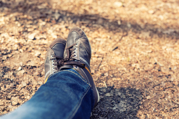 Ormanda yürüyüş sonra dinlenme. Yakın çekim bacaklar rahat mavi jeans ve kahverengi deri çizme. Macera ve seyahat kavramı - Fotoğraf, Görsel