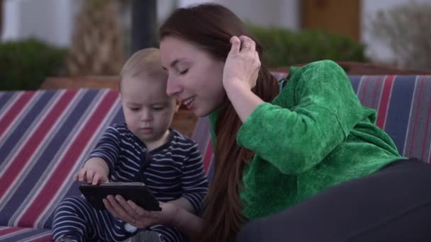 De baby klikt op de smartphone, zittend met zijn moeder in slow motion. - Video