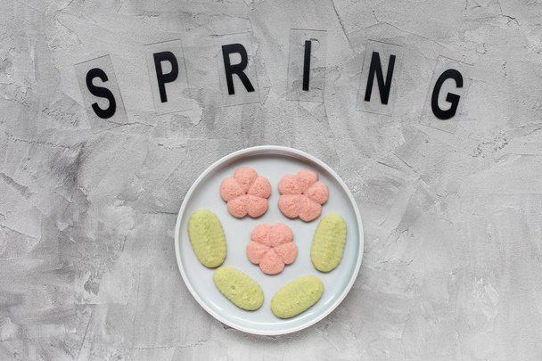 Άνοιξη cookies λέξη και λουλούδι σε ένα πιάτο σε ένα γκρίζο φόντο . - Φωτογραφία, εικόνα