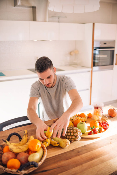 Young and healthy man putting fruits in his blender early in the - Foto, immagini