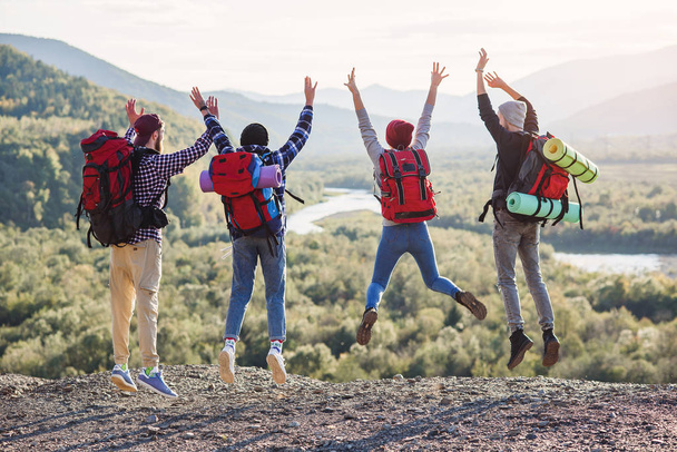 Group of five happy friends jumps at sunset time on background mountains - 写真・画像