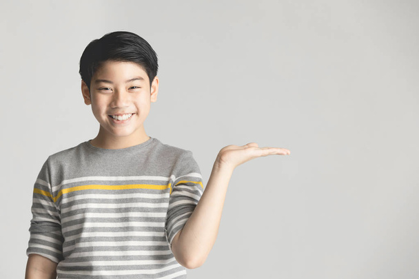 Asian preteen presenting something on hand over gray background. - Foto, Imagen