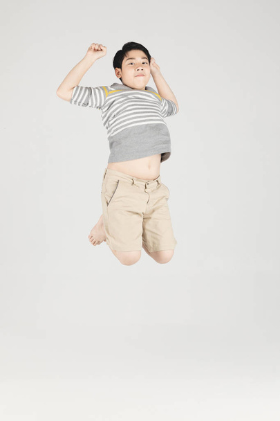 Asian śmieszne dziecko chłopiec skoki na szarym tle. - Zdjęcie, obraz