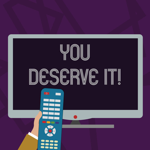Text sign showing You Deserve It. Conceptual photo should have it because of their qualities or actions Hand Holding Computer Remote Control infront of Blank Wide Color PC Screen. - Photo, Image