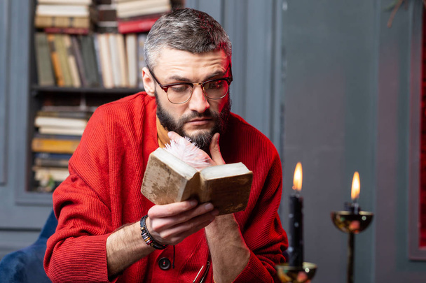 Future predictor wearing glasses reading little old book about divination - Fotografie, Obrázek